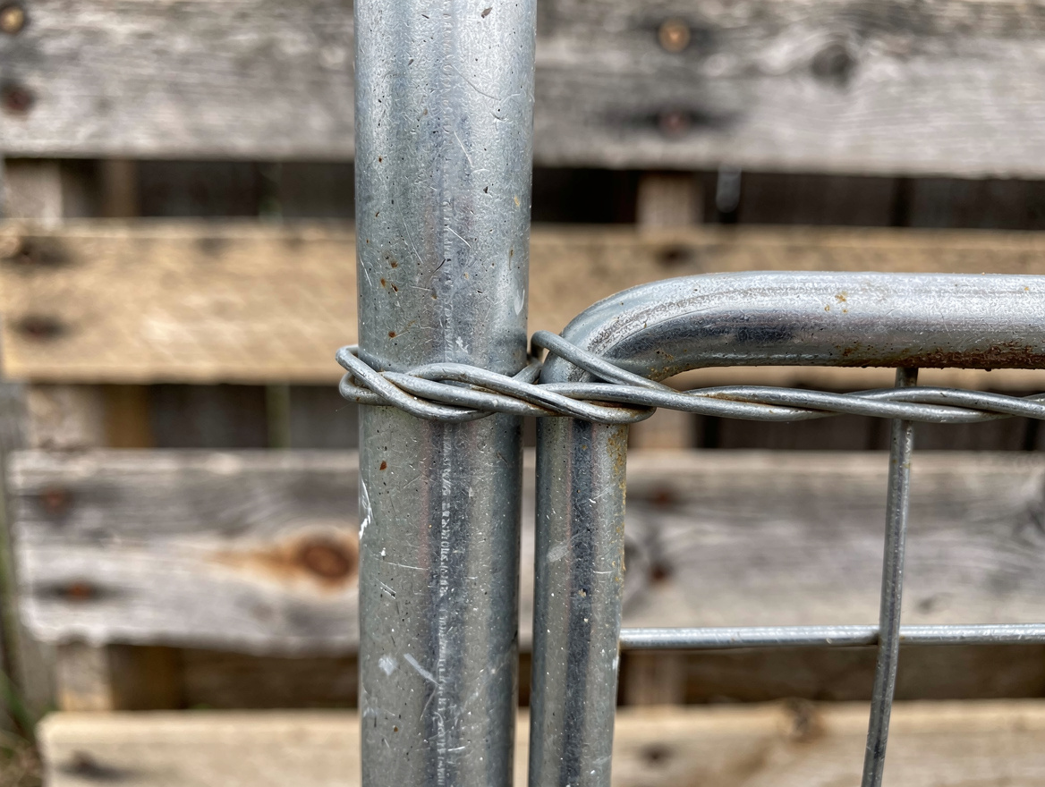 Close-up detail photo of galvanized wire, steel T-post, and cattle panel connect