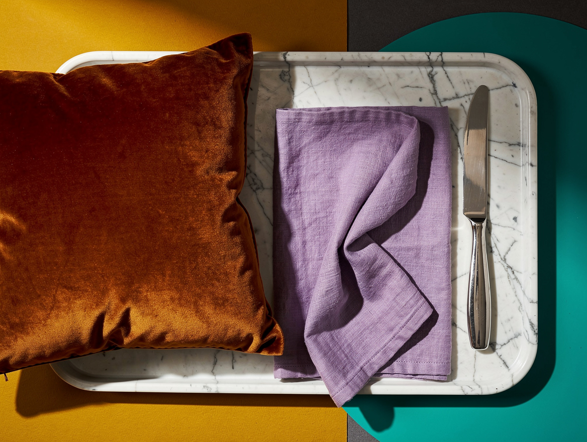 overhead flat lay of a velvet rust pillow, a lavender linen napkin, and a chrome