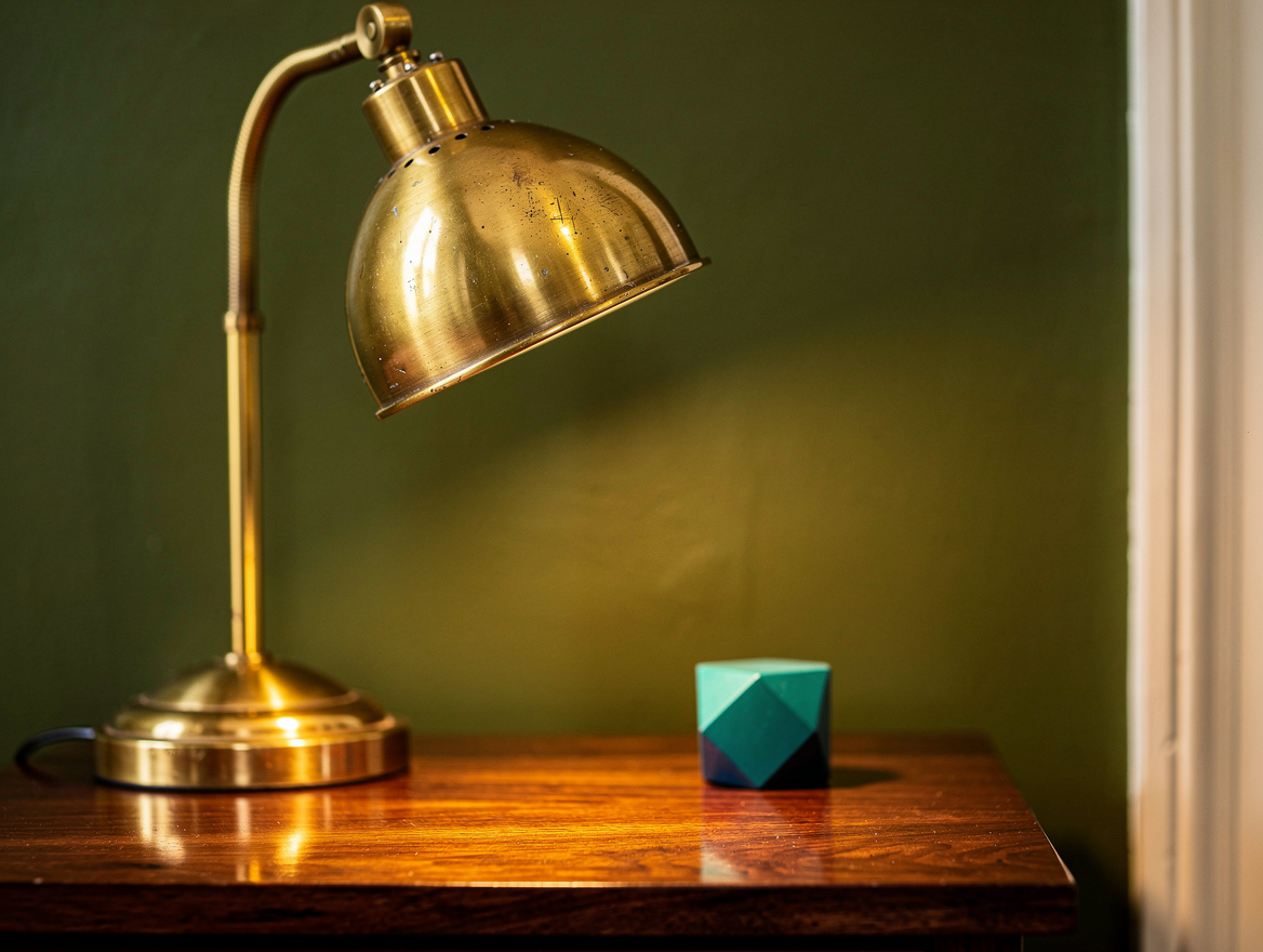 Editorial close-up detail of an aged brass bedside lamp against deep olive matte