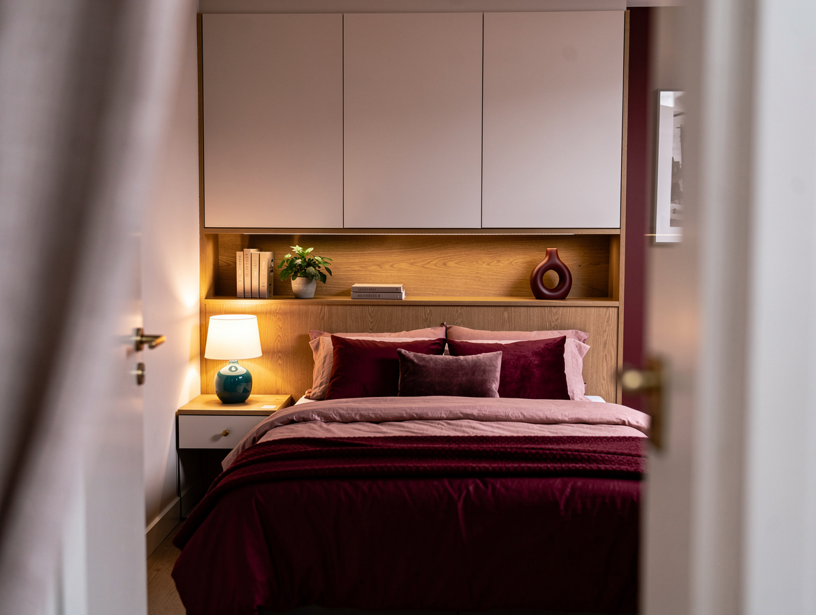 Wide atmospheric photo of a narrow bedroom with a queen bed, slim oak headboard