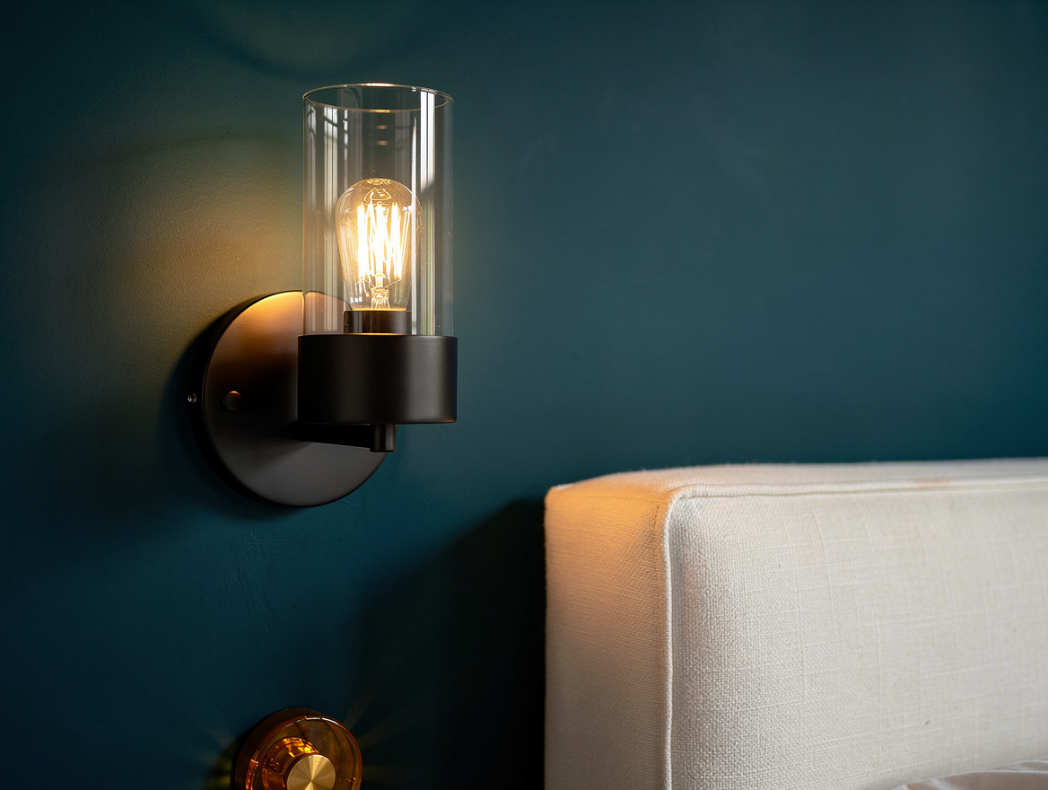 Close detail photo of a matte black wall sconce with a cylindrical clear glass s