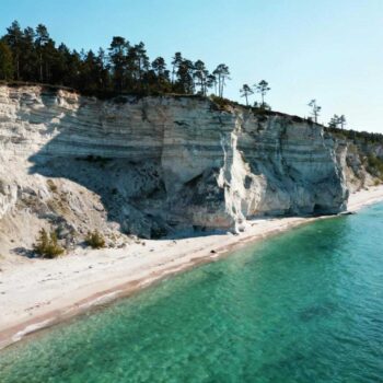 De veerboot vertrekt om 08:00 uit Virtsu haven. Dertig minuten later bereik je Saaremaa, Estland's grootste eiland met 2.673 km² ongerepte natuur. Terwijl Tallinn jaarlijks 5 miljoen bezoekers verwerkt, trekt dit paradijs slechts 150.000 reizigers. Sparrenbossen bedekken 54% van het eiland. Kalksteenkliffen kantelen de kustlijn. Rieten daken glanzen tussen eeuwenoude eiken. De 31.000 inwoners koesteren hun isolatie als een kostbaar geheim. De 30-minuten overtocht die alles verandert De veerboot van TS Laevad vaart 19 keer per dag tussen Virtsu en Kuivastu. Een overtocht kost €4,50 per persoon in november 2025. Auto's betalen €15,00 extra. De 7,8 kilometer lange reis onthult geen hotelcomplexen op de horizon. Kuressaare verschijnt als een middeleeuwse verrassing. Geen high-rise hotels doorprikken de skyline. Het 14e-eeuwse kasteel domineert het stadscentrum. Bloeiende lindebomen omringen stenen straten. Toeristen lopen er niet schouder aan schouder. De Muhu-dam verbindt het eiland met het vasteland. Dichte sparrenbossen flankeren de verharde weg. Rieten daken gluren tussen groene takken. Deze architectuur dateert uit de 18e eeuw. Meer dan authentieke Baltische erfgoed vind je nergens anders. Wat 150.000 jaarlijkse bezoekers verspreid over 2.673 km² betekent Saaremaa registreert 0,056 bezoekers per vierkante kilometer. Tallinn's oude stad pakt 15.000 dagelijkse bezoekers op 1,3 km². Het contrast definieert wat echte ruimte betekent in 2025. Kaali meteorietkrater: 5 miljoen jaar geheim Europa's eerste wetenschappelijk erkende meteorietinslag ligt 20 kilometer van Kuressaare. De krater meet 110 meter in diameter. Blauwgroen water vult de cirkel. Geen entreepoort verspert de toegang. Dagelijks bezoeken 25 mensen de krater in november. Augustusmaanden trekken 200 bezoekers per dag. Lokale vogelaars kennen de beste observatieplekken. Toeristen fotograferen. Bewoners leven gewoon verder. Angla windmolens: ambachtelijk erfgoed zonder stickers Vijf houten windmolens uit de 19e eeuw draaien nog steeds. Twee molens functioneren volledig. Demonstraties vinden plaats op woensdag en zaterdag van 11:00 tot 14:00. Handgesneden wieken worden elke vijf jaar vernieuwd. Lokale ambachtslieden gebruiken traditionele Saaremaa-houtsoorten. Geen TripAdvisor-certificaten hangen aan de deur. Bezoekers betalen €3,00 toegang. Het geld ondersteunt onderhoud, niet marketing. De €60-120 accommodatie realiteit die Tallinn vergeet Familiegerunde guesthouses bieden kamers voor €65 per nacht in november. Tallinn centrum vraagt €120 voor vergelijkbare kwaliteit. Rieten daken beschermen authentieke interieurs. Zelfgebakken roggebrood wacht bij het ontbijt. Overnachten in rieten dak guesthouses Saaremaa Rahvus accepteert maximaal 4 gasten per week. Eigenaren selecteren bezoekers op motivatie. Authentieke gastvrijheid vervangt minibar-service. Handgetekende wandelkaarten tonen geheime paden. Panga Peremeus biedt 3 kamers met uitzicht op de Baltische Zee. Zonsondergangwandelingen zijn inbegrepen. Geen televisies verstoren de natuurlijke stilte. Rustige waterlocaties blijven zo beschermd. Saaremaa-bier en wildgerechten Lokale brouwerijen produceren ambachtelijk bier sinds 1850. Wild zwijn kost €14 in dorpsrestaurants. Tallinn vraagt €28 voor hetzelfde gerecht. Bospaddestoelen groeien vrij langs wandelpaden. Kuressaare Kohvik serveert kama, een mengsel van geroosterde granen. Räim is gebakken visbrood met plaatselijke vis. Saaremaa kaas bevat kruidnagel uit lokale productie. Toeristen proeven, locals eten dagelijks. De stilte die je alleen hoort als massa's wegblijven Ochtendfietsers rijden langs verlaten kustlijnen. Krijsende meeuwen vormen de enige soundtrack. Windmolens draaien in de Baltische wind. Zonsondergangen bij Panga-kliffen gebeuren zonder mensenmassa's. Dit is authenticiteit in 2025: niet gereconstrueerd voor Instagram. Lokale trots beschermt het eiland. Bewoners leven gewoon. Ze poseren niet voor bezoekers. Verborgen Noord-Europese parels bestaan nog steeds. Tiina Saar van Visit Saaremaa legt uit: "Onze focus ligt op duurzaam toerisme. Bezoekers en bewoners moeten profiteren van authentieke ervaringen met respect voor natuur en cultuur." Jouw vragen over Saaremaa, Estland – eiland van vuurtorens en bossen beantwoord Wat is de goedkoopste manier om Saaremaa te bereiken vanuit Nederland? Vlieg naar Tallinn vanaf €150 retour. Neem de bus naar Virtsu haven (€15, 4 uur totaal). De veerboot kost €4,50 per persoon. Totale reiskosten blijven onder €170. Seizoentiming beïnvloedt vliegprijzen significant. Waarom bezoeken zo weinig toeristen Saaremaa vergeleken met Tallinn? De veerbootafhankelijkheid houdt massa's weg. Beperkte internationale marketing is bewust beleid. Locals prefereren 150.000 jaarlijkse bezoekers boven Tallinn's 5 miljoen. Anna Mänd, reisblogger, zegt: "Voor ongerepte Baltische ervaringen is Saaremaa perfect." Hoe vergelijkt Saaremaa met Gotland of andere eilanden? Saaremaa biedt 40% lagere kosten dan Gotland. Accommodaties kosten €60-120 versus €150+. Gotland registreert 1,8 miljoen jaarlijkse bezoekers. Saaremaa blijft authentiek met meteorietkrater, middeleeuwse burcht en Baltische flora. Commercialisatie blijft beperkt. De laatste veerboot vertrekt om 21:00 terug naar het vasteland. Drie locals staan naast je die familiebezoek hebben afgelegd. Niemand fotografeert de zonsondergang boven de Baltische Zee. Saaremaa bestaat simpelweg, zonder te poseren voor camera's.