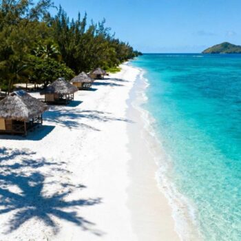Drie beach fales staan op wit zand, palmbomen wuiven in de Stille Oceaan-wind. Turquoise water strekt zich uit naar Nu'utele eiland. Lalomanu Beach vraagt € 18 toegang terwijl Bora Bora resorts honderden euro's rekenen per nacht. Dit Samoaanse strand onthult wat commerciële bestemmingen verbergen. Authentieke Polynesische ervaringen kosten weinig maar bieden ongerepte schoonheid. Culturele diepgang die geen luxeresort kan evenaren. Aankomst in Samoa's zuidoostelijke paradijs De rit van Apia duurt 75 minuten over verharde wegen. Eerste glimp van 1,5 km wit zandstrand verschijnt achter tropische vegetatie. Traditionele beach fales markeren de kustlijn als rieten monumenten. Het contrast verbaast bezoekers onmiddellijk. Goedkoop betekent hier niet minder mooi. Het strand rivaliseert met Bora Bora maar zonder de mensenmassa's. Slechts 20.000 bezoekers per jaar versus 120.000 in Frans-Polynesië. Lokale families beheren de toegang zelf. Het € 18 entreegeld ondersteunt direct 712 inwoners. Geen corporate keten maar gemeenschapstoerisme sinds de tsunami-wederopbouw van 2009. Zeven gratis ervaringen die resorts niet bieden Het toegangsgeld van 50 WST opent meer dan strandzand. Het onthult een wereld van authentieke Polynesische cultuur. Lokale wijsheid wordt gratis gedeeld met respectvolle bezoekers. Snorkelen in ongerepte lagune Kristalhelder water heeft 25-30 meter zichtbaarheid tijdens het droge seizoen. Koraalriffen beginnen op 50 meter van het strand. Clownvissen, parrotfish en groene schildpadden zwemmen tussen staghorn koraal. Geen geleide tours nodig of dure bootuitstapjes. Eigen snorkeluitrusting kost € 6 per dag huur. Gratis wateractiviteiten maken het verschil met commerciële bestemmingen. Beach fale culturele onderdompeling Traditionele rieten hutten kosten € 50-84 per nacht inclusief maaltijden. Open constructie zonder muren biedt directe verbinding met de oceaan. Muggennet beschermt tegen tropische insecten terwijl zeewind verkoeling brengt. Gemeenschappelijke badkamers liggen 20 meter verderop. Eenvoud en authenticiteit vervangen luxe amenities. Slapen onder Stille Oceaan-sterren zonder hotelbarrières. Wat locals echt eten versus resort menu's Samoaanse families delen hun keuken met gasten. Geen toeristische voorstellingen maar dagelijks leven. Traditionele gerechten kosten € 4-17 per maaltijd. Verse vis plus kokosgerechten voor € 5-15 Palusami combineert taro met kokosmelk voor € 5,70. Tataki marineert verse vis in citrus voor € 9,50. Broodfruit wordt gebakken voor € 3,80. Dezelfde gerechten kosten € 25-35 in Bora Bora resorts. Taufua Beach Fales Restaurant serveert van 7:00 tot 21:00. Alleen contant betalen in WST. Ingrediënten komen van eigen tuinen en lokale vissers. Traditionele kookdemonstraties Lokale families gebruiken 'umu aardovens dagelijks om 15:00. Geen theatrale voorstelling maar praktische voedselvoorbereiding. Bezoekers observeren en leren gratis tijdens hun verblijf. Fa'ausi bananendessert wordt bereid met kokosroom. Lokale eetcultuur onthult authentieke smaken die toeristen anders missen. De € 18 die toerisme anders maakt Het strandtoeganggeld financiert meer dan onderhoud. Onderwijsbeurzen voor 15 lokale kinderen worden mogelijk. Koraalherstelprojecten beschermen het ecosysteem. Lokale veiligheidsdienst bewaakt 2 km kustlijn. Fa'a Samoa leefwijze draait om wederzijds respect. Toeristen worden uitgenodigd in het gemeenschapsleven. Geen commerciële transactie maar culturele uitwisseling. Zoals lokale gids Maia Tui zegt: "Lalomanu draagt de verhalen van onze voorvaderen." Zonsondergang kleurt Nu'utele eiland oranje terwijl vissers prauwen naar strand trekken. Budget-bewuste lokale strategieën maken authentieke ervaringen toegankelijk. Jouw vragen over Lalomanu Beach, Samoa beantwoord Wat is de beste tijd om Lalomanu Beach te bezoeken? Mei tot oktober biedt 24-30°C temperaturen met minimale neerslag. Waterzichtbaarheid bereikt 30 meter tijdens deze maanden. Droge seizoen vermijdt cycloonrisico en biedt perfecte snorkelcondities. Hoe ervaar ik Fa'a Samoa respectvol als toerist? Bedek schouders en knieën in het dorp. Vraag toestemming voor foto's van lokale bewoners. Deel maaltijden in fale-stijl wanneer uitgenodigd. Leer "Talofa" (hallo) en "Fa'afetai" (dank je wel) in het Samoaans. Hoe verschilt Lalomanu van Bora Bora of Maui? Lalomanu verwelkomt 20.000 bezoekers jaarlijks versus 2,7 miljoen op Maui. Accommodaties kosten € 50-84 inclusief maaltijden versus € 800-1200 op Bora Bora. Timing-geheimen maken het verschil voor authentieke ervaringen. Een Samoaanse familie deelt kokosnoot bij de beach fale. Vissers sorteren vangst op het zand. Dit is Lalomanu's geheim: echte Polynesische gastvrijheid kost weinig maar geeft wat geen resort kan kopen.