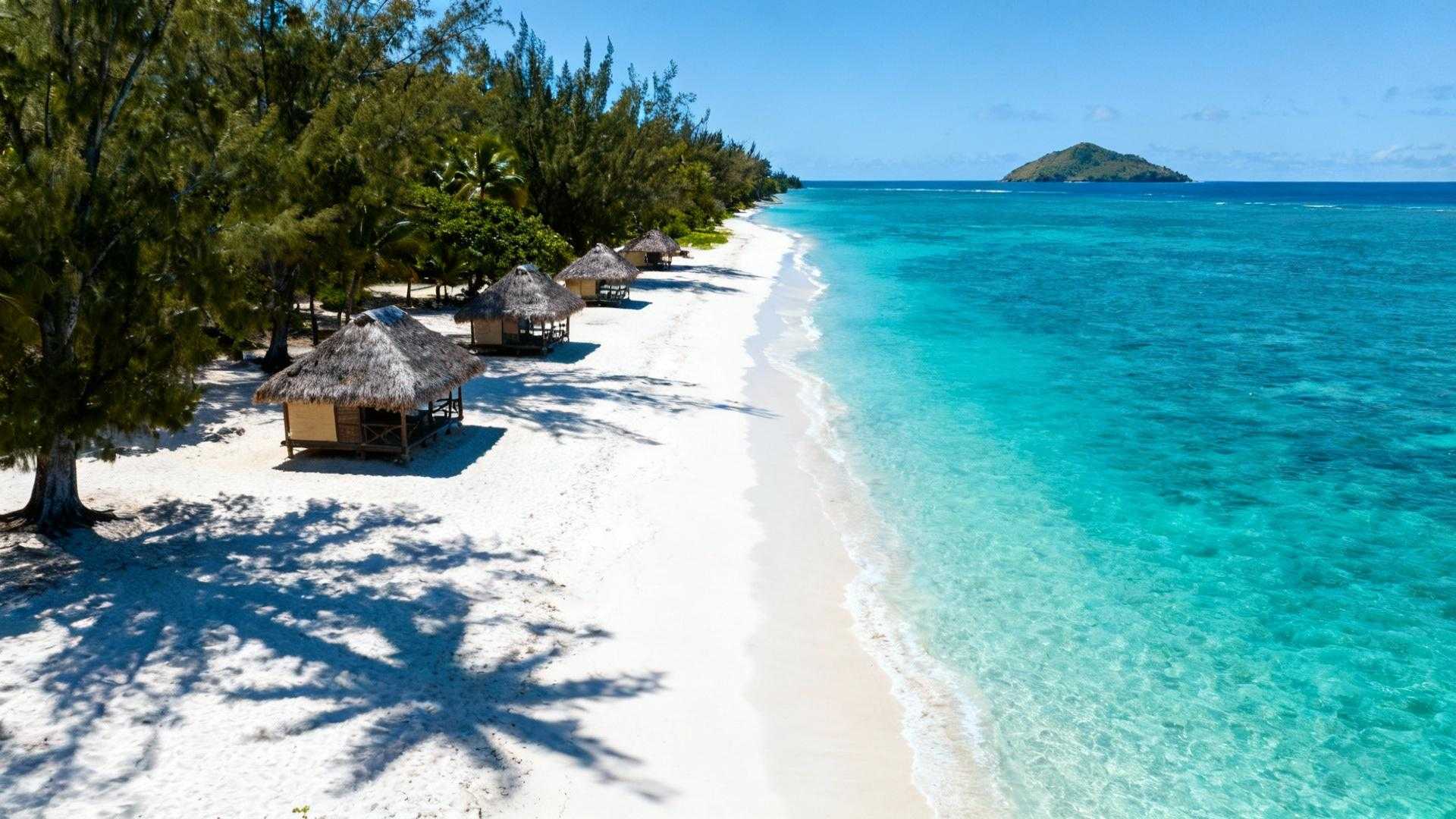 Drie beach fales staan op wit zand, palmbomen wuiven in de Stille Oceaan-wind. Turquoise water strekt zich uit naar Nu'utele eiland. Lalomanu Beach vraagt € 18 toegang terwijl Bora Bora resorts honderden euro's rekenen per nacht. Dit Samoaanse strand onthult wat commerciële bestemmingen verbergen. Authentieke Polynesische ervaringen kosten weinig maar bieden ongerepte schoonheid. Culturele diepgang die geen luxeresort kan evenaren. Aankomst in Samoa's zuidoostelijke paradijs De rit van Apia duurt 75 minuten over verharde wegen. Eerste glimp van 1,5 km wit zandstrand verschijnt achter tropische vegetatie. Traditionele beach fales markeren de kustlijn als rieten monumenten. Het contrast verbaast bezoekers onmiddellijk. Goedkoop betekent hier niet minder mooi. Het strand rivaliseert met Bora Bora maar zonder de mensenmassa's. Slechts 20.000 bezoekers per jaar versus 120.000 in Frans-Polynesië. Lokale families beheren de toegang zelf. Het € 18 entreegeld ondersteunt direct 712 inwoners. Geen corporate keten maar gemeenschapstoerisme sinds de tsunami-wederopbouw van 2009. Zeven gratis ervaringen die resorts niet bieden Het toegangsgeld van 50 WST opent meer dan strandzand. Het onthult een wereld van authentieke Polynesische cultuur. Lokale wijsheid wordt gratis gedeeld met respectvolle bezoekers. Snorkelen in ongerepte lagune Kristalhelder water heeft 25-30 meter zichtbaarheid tijdens het droge seizoen. Koraalriffen beginnen op 50 meter van het strand. Clownvissen, parrotfish en groene schildpadden zwemmen tussen staghorn koraal. Geen geleide tours nodig of dure bootuitstapjes. Eigen snorkeluitrusting kost € 6 per dag huur. Gratis wateractiviteiten maken het verschil met commerciële bestemmingen. Beach fale culturele onderdompeling Traditionele rieten hutten kosten € 50-84 per nacht inclusief maaltijden. Open constructie zonder muren biedt directe verbinding met de oceaan. Muggennet beschermt tegen tropische insecten terwijl zeewind verkoeling brengt. Gemeenschappelijke badkamers liggen 20 meter verderop. Eenvoud en authenticiteit vervangen luxe amenities. Slapen onder Stille Oceaan-sterren zonder hotelbarrières. Wat locals echt eten versus resort menu's Samoaanse families delen hun keuken met gasten. Geen toeristische voorstellingen maar dagelijks leven. Traditionele gerechten kosten € 4-17 per maaltijd. Verse vis plus kokosgerechten voor € 5-15 Palusami combineert taro met kokosmelk voor € 5,70. Tataki marineert verse vis in citrus voor € 9,50. Broodfruit wordt gebakken voor € 3,80. Dezelfde gerechten kosten € 25-35 in Bora Bora resorts. Taufua Beach Fales Restaurant serveert van 7:00 tot 21:00. Alleen contant betalen in WST. Ingrediënten komen van eigen tuinen en lokale vissers. Traditionele kookdemonstraties Lokale families gebruiken 'umu aardovens dagelijks om 15:00. Geen theatrale voorstelling maar praktische voedselvoorbereiding. Bezoekers observeren en leren gratis tijdens hun verblijf. Fa'ausi bananendessert wordt bereid met kokosroom. Lokale eetcultuur onthult authentieke smaken die toeristen anders missen. De € 18 die toerisme anders maakt Het strandtoeganggeld financiert meer dan onderhoud. Onderwijsbeurzen voor 15 lokale kinderen worden mogelijk. Koraalherstelprojecten beschermen het ecosysteem. Lokale veiligheidsdienst bewaakt 2 km kustlijn. Fa'a Samoa leefwijze draait om wederzijds respect. Toeristen worden uitgenodigd in het gemeenschapsleven. Geen commerciële transactie maar culturele uitwisseling. Zoals lokale gids Maia Tui zegt: "Lalomanu draagt de verhalen van onze voorvaderen." Zonsondergang kleurt Nu'utele eiland oranje terwijl vissers prauwen naar strand trekken. Budget-bewuste lokale strategieën maken authentieke ervaringen toegankelijk. Jouw vragen over Lalomanu Beach, Samoa beantwoord Wat is de beste tijd om Lalomanu Beach te bezoeken? Mei tot oktober biedt 24-30°C temperaturen met minimale neerslag. Waterzichtbaarheid bereikt 30 meter tijdens deze maanden. Droge seizoen vermijdt cycloonrisico en biedt perfecte snorkelcondities. Hoe ervaar ik Fa'a Samoa respectvol als toerist? Bedek schouders en knieën in het dorp. Vraag toestemming voor foto's van lokale bewoners. Deel maaltijden in fale-stijl wanneer uitgenodigd. Leer "Talofa" (hallo) en "Fa'afetai" (dank je wel) in het Samoaans. Hoe verschilt Lalomanu van Bora Bora of Maui? Lalomanu verwelkomt 20.000 bezoekers jaarlijks versus 2,7 miljoen op Maui. Accommodaties kosten € 50-84 inclusief maaltijden versus € 800-1200 op Bora Bora. Timing-geheimen maken het verschil voor authentieke ervaringen. Een Samoaanse familie deelt kokosnoot bij de beach fale. Vissers sorteren vangst op het zand. Dit is Lalomanu's geheim: echte Polynesische gastvrijheid kost weinig maar geeft wat geen resort kan kopen.