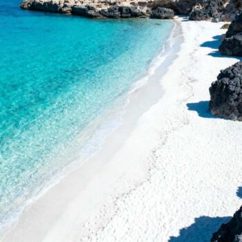 Augustusmiddag op Spiaggia dei Conigli. De 547ste bezoeker van de dag fotografeert turquoise water zonder op te merken dat de 6.000 Lampedusa-bewoners het strand al om 17:00 verlaten. Dit beschermde natuurreservaat sinds 2006 heeft ongeschreven regels die toeristen nooit begrijpen. Het reserveringssysteem lijkt simpel: €1,30 voor twee personen, maximaal 550 bezoekers per shift. Maar locals weten dat deze 200 meter lange baai meer vereist dan een online booking. De reservering betekent meer dan toegang — het is jouw contract met natuur Maria Carmela Vassallo benadrukt: "Vanaf juni tot oktober geldt een streng toegangsbeleid voor Spiaggia dei Conigli, met slechts 550 bezoekers per tijdslot. Dit om het delicate ecosysteem van schildpadden te beschermen." Toeristen zien het als formaliteit. Lampedusa-bewoners beschouwen het als privilege dat je verdient door correct gedrag. De twee shifts (8:30-13:30 en 14:30-19:30) beschermen niet alleen Caretta caretta nesting, maar behouden de sereniteit die massatoerisme vernietigt. Echte insiders weten: reserveer voor de vroege ochtendshift. De eerste 50 bezoekers ervaren het strand zoals bedoeld — zonder drukte, met perfect licht voor de turquoise kleuren die het internationale roem gaven. Het 800 meter wandelpad test jouw intenties Luca Gallo verklaart: "Het pad naar het strand biedt adembenemende uitzichten en bereidt je voor op een tocht door een van de meest ongerepte natuurgebieden van Italië." Waarom goede schoenen geen suggestie zijn De 800 meter vanaf de parkeerplaats is geen ongemak — het is opzettelijk filter. Geen auto-toegang voorkomt commercialisering. Locals observeren hoe bezoekers het pad benaderen: wie klaagt over de afstand, wie onvoorbereid struikelt in teenslippers. Het panoramische uitzicht onderweg toont grillige vulkanische rotsen en kristalhelder water. Maar alleen als je niet gehaast bent naar de Instagram-foto. Matera heeft 150 rotskerken waar 98% van 1,5 miljoen bezoekers de fresco's mist — hetzelfde patroon van gemiste diepgang door haast. Het pad ritueel betekent timing Bewoners wandelen bij zonsopgang (06:30) of na 17:00. Middag-hitte van 32°C in augustus is toeristentijd. De temperatuur vertelt wanneer locals vertrekken — en waarom respectvolle bezoekers hetzelfde doen. Caretta caretta etiquette — wat bordjes niet uitleggen De nestelingsperiode is heilig tussen mei en augustus Het reserveringssysteem sluit om 19:00 niet voor administratie — het beschermt nesting-uren. Zeeschildpadden verkennen het gebied bij schemering. Geen flitsfotografie. Geen strandballen die trillingen veroorzaken in het zand waar eieren liggen. Marco Fontana bevestigt: "Door de strikte beperkingen is de biodiversiteit rond Spiaggia dei Conigli met succes hersteld, een voorbeeld voor het beheer van kwetsbare toeristische gebieden." Locals vertellen het nooit direct — ze verwachten dat respectvolle bezoekers het begrijpen. La Pelosa op Sardinië heeft vergelijkbare beschermingsregels voor Mediterraan strandecosysteem. Zwemmen heeft onzichtbare grenzen Het kleine eilandje Isola dei Conigli, 100 meter voor de kust, lijkt bereikbaar. Maar locals zwemmen er nooit naartoe tijdens nesting-maanden — het eiland is beschermd Caretta caretta gebied. De stromingen zijn verraderlijk zonder lifeguards. Bewoners houden oogcontact met zwemmers — niet controle, maar zorgattentie die generaties Lampedusa-families kenmerkt sinds de natuurreservaat-status van 2006. De onzichtbare vuile was-test onthult respect Anna Russo merkt op: "Lampedusa en het Spiaggia dei Conigli zijn verborgen juweeltjes, met turquoise zee en weinig massatoerisme vergeleken met andere bestemmingen in de Middellandse Zee." Elke dag na 19:00 sluitingstijd inspecteren locals het strand. Het verschil tussen "schoon achtergelaten" en "perfect ongerept" bepaalt hoe bewoners over toerisme denken. Geen prullenbakken is geen gebrek — het is filosofie. Plastic flessen, sigarettenpeuken, voedselresten: elk stuk afval voelt als persoonlijke belediging aan het 19-jaar natuurbehoud. Phra Nang Cave Beach heeft identieke onuitgesproken regels voor beschermde natuurgebieden. Jouw vragen over Spiaggia dei Conigli (Plage des Lapins), Lampedusa (Italie) beantwoord Moet ik echt reserveren, zelfs in mei? Ja. Het systeem draait juni-oktober officieel, maar mei-reservering wordt sterk aangeraden. Het voorkomt teleurstelling bij de 550-limiet en toont respect voor beheersysteem. Reserveer via prenotazionespiaggiaconigli.it minimaal 48 uur vooraf. Toegang is tijdelijk gratis in 2025 tijdens systeemaanpassingen. Waarom vertrekken locals om 17:00? Niet vanwege sluitingstijd (19:00), maar vanwege respect voor schemerperiode wanneer zeeschildpadden gebied verkennen voor nesting. Locals ervaren het strand in twee shifts die toeristen missen: 06:30-09:00 zonsopgang-rust en 17:30-19:00 gouden uur-sereniteit. Loire-kastelen hebben vergelijkbare timing-strategieën voor beschermde toegang. Is het echt mooier dan andere middellandse zee stranden? Objectief: TripAdvisor Top 10 wereldwijd, Legambiente-erkenning voor waterkwaliteit. De combinatie van beschermingsstatus, bezoekerslimieten en actieve natuurbehoud creëert atmosfeer die gecommercialiseerde stranden verloren. Spiaggia dei Conigli voelt authentieker door gedwongen bezoekerslimieten dan Cala Mariolu of Palombaggia. 18:45 uur. De laatste toerist vertrekt. Een Lampedusa-vrouw wandelt het 800 meter pad met rieten mand, verzamelt achtergebleven plastic. Ze groet twee vroege bezoekers voor volgende dag: "Domani, alle sei e mezzo — il mare è vostro." Morgen, 06:30 — de zee is van jullie. Maar alleen als je de ongeschreven regels kent.